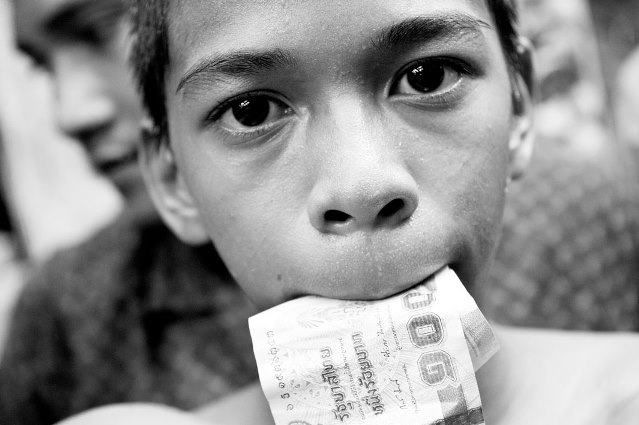 A boy with money in his mouth. After winning the boxing match winner goes around and collects money from tourists certificates. After that, the money is divided, the coach gets the largest share.
